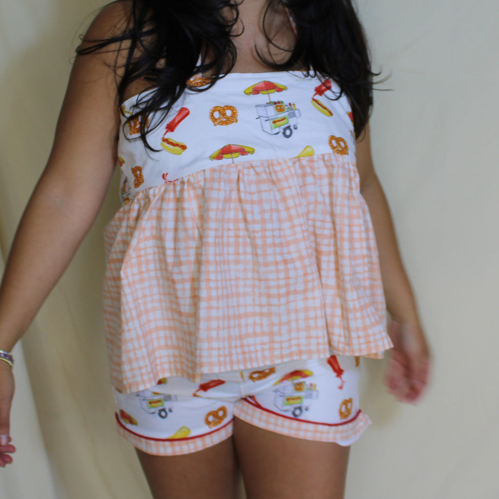 Woman wearing a peach gingham babydoll halter top with playful snack-print bust panel featuring hotdogs, pretzels, and condiments. Ethically handmade summer top from upcycled deadstock fabric, styled against a neutral backdrop. 