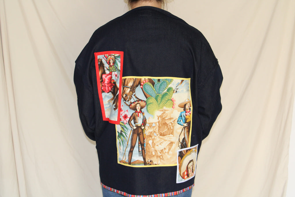 Handmade black denim jacket featuring a large western cowgirl collage patch on the back with vintage rodeo artwork and desert motifs. Accented with colorful serape trim along the hem and crafted from upcycled materials for a bold, sustainable statement. 