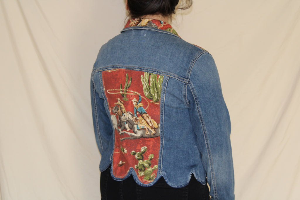 Upcycled denim jacket with scalloped hem and a bold red vintage cowboy panel on the back. Features a lassoing rodeo rider and cactus print, finished with a western-inspired collar and contrast stitching. Handmade for a one-of-a-kind, sustainable statement piece. 