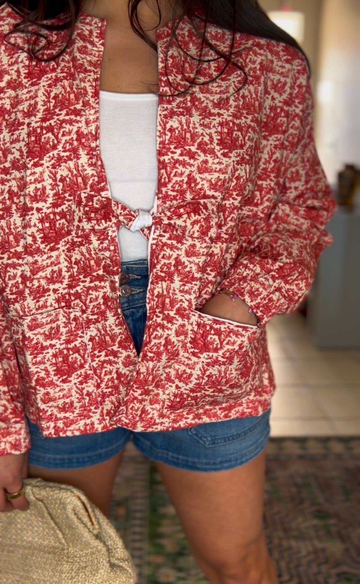 Handmade jacket featuring a red miniature toile de Jouy print on a soft cotton. Designed with roomy front pockets and an open front, and a subtle waist tie for easy layering. Ethically made in the USA from upcycled deadstock fabric. Classic with a playful twist-pairs perfectly with denim or dresses. 