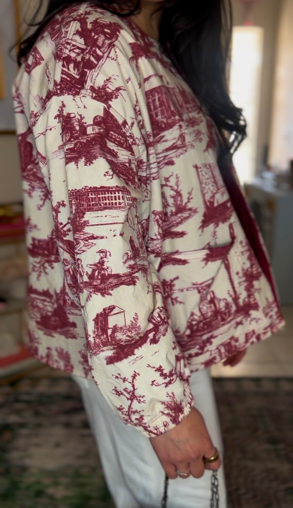 Handmade French toile jacket in vintage maroon and cream, featuring countryside rodeo scenes, raw edges, and a structured silhouette. Cut from rare deadstock upholstery fabric. 